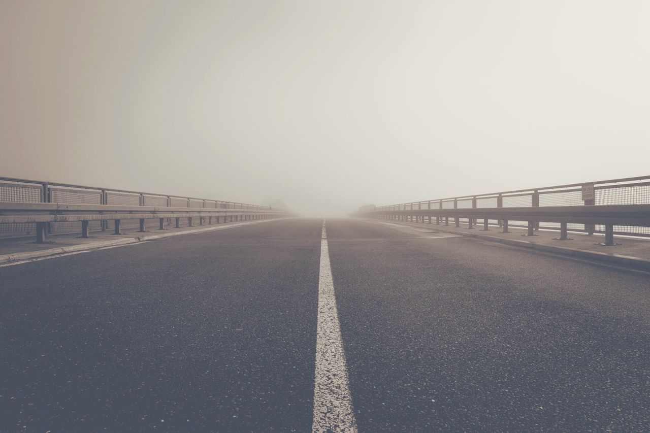 Pont désert noyé de brume, ligne blanche centrale fuyant vers l'horizon pâle