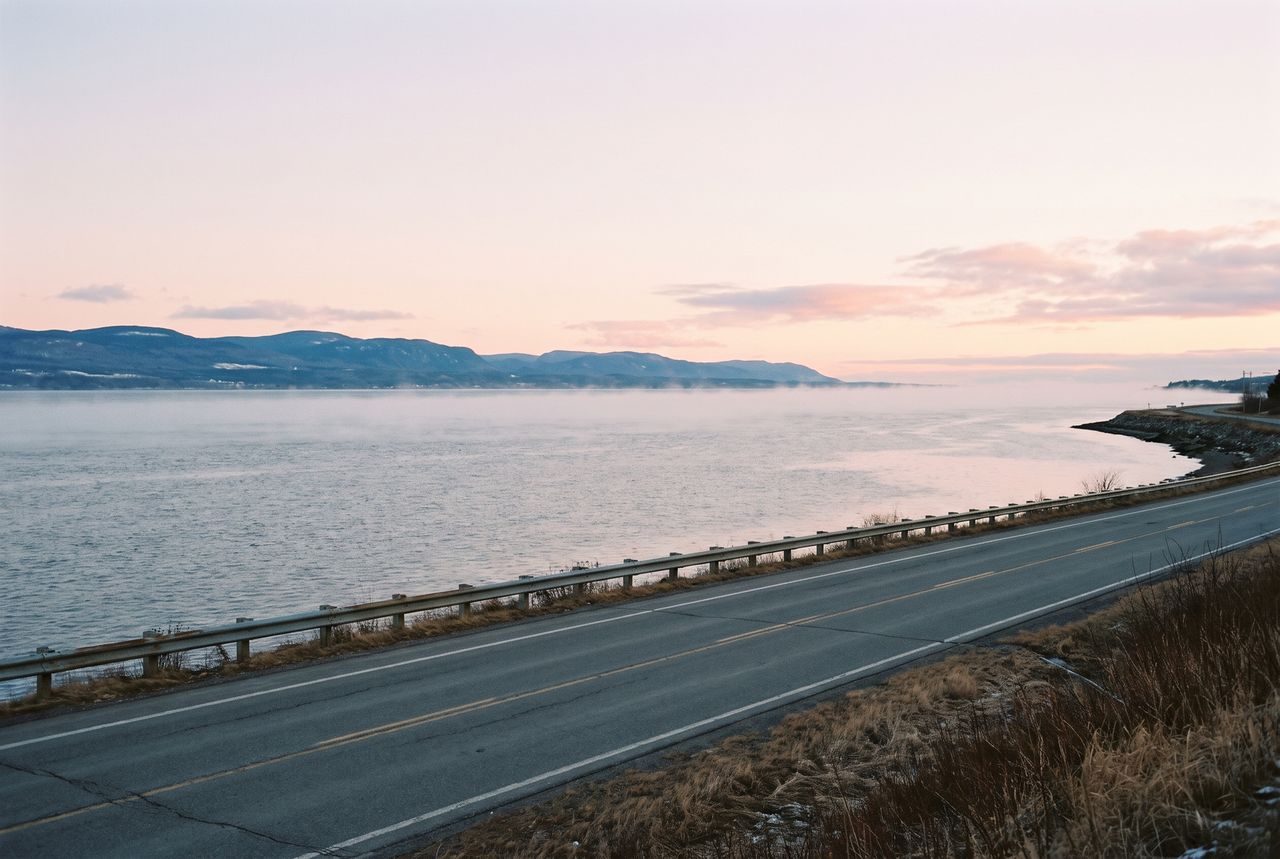 Estuaire du Saint-Laurent à l'aube, brume sur l'eau, montagnes au loin et route côtière déserte